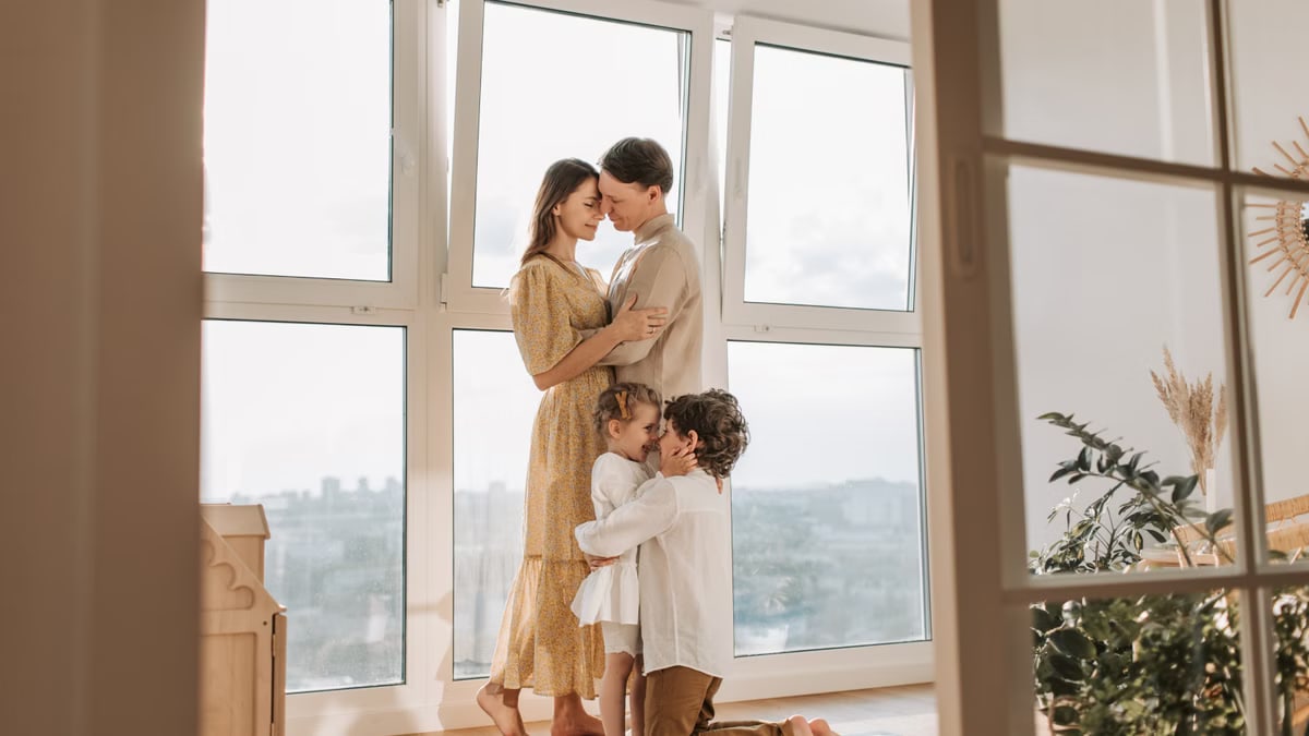A loving family shares an affectionate moment near a bright window.